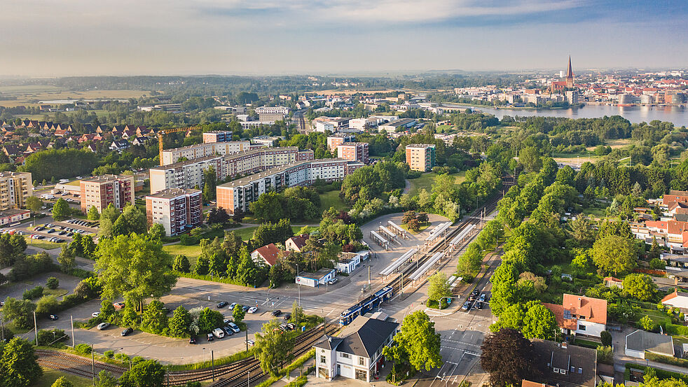 Luftaufnahme von Rostock mit Wohnblocks, Straßenbahn-Depot und viel Grün im Vordergrund, dahinter die Altstadt mit der Petrikirche am Ufer der Warnow.
